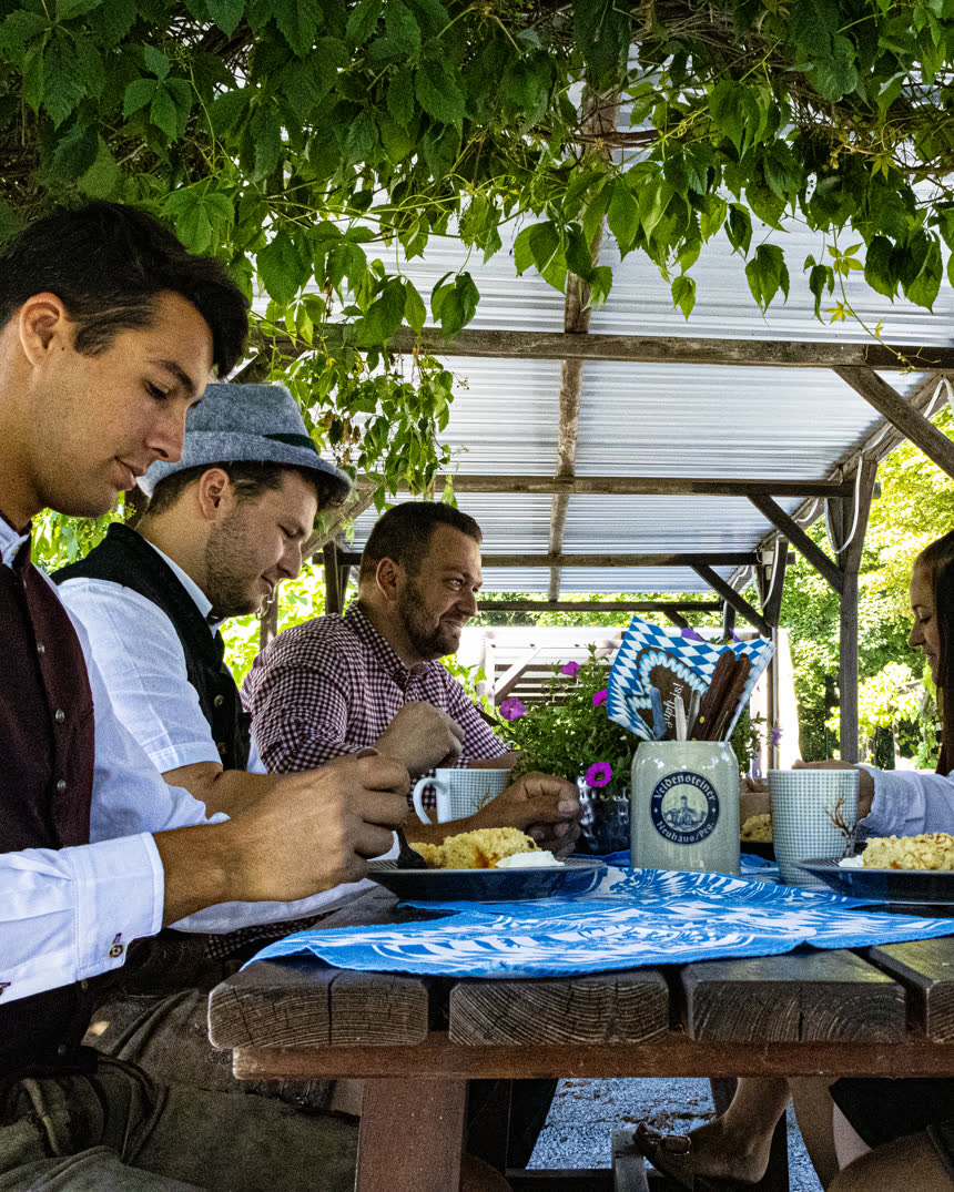 Gäste bei der Brotzeit unter der berankten Pergola des Biergartens